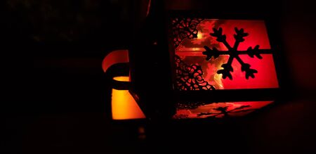 a red candlestick in the form of a house with snowflakes on a black background and another candle is burningの写真素材