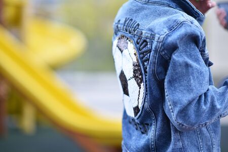 back view of smart casual boy in blue jeans shirt looking up and holding hands in pockets, black and white soccer ball on the shirt is drawnの写真素材