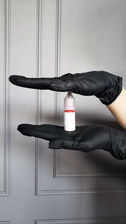 Hand in protective blue glove holding empty bottle. Small plastic container with cup. Isolated on grey background.の写真素材