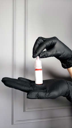 Hand in protective blue glove holding empty bottle. Small plastic container with cup. Isolated on grey background.の写真素材