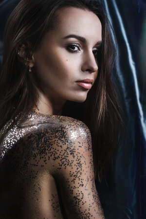 Portrait of a girl with makeup and sequins on her body. Evening make-up in the studio. Covering the body with glitter. Anxious body.の写真素材