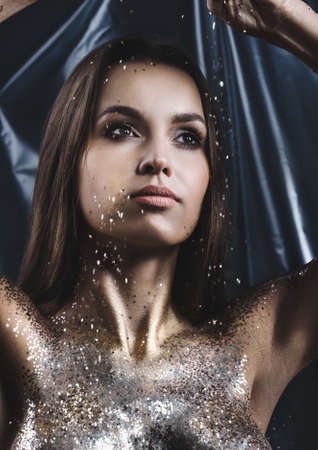 Portrait of a girl with makeup and sequins on her body. Evening make-up in the studio. Covering the body with glitter. Anxious body.の写真素材