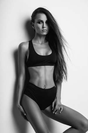 black and white studio photo. Girl model with long hair posing in the studio on a light background. The girl is dressed in short black shorts and a T-shirt. fitness body.の写真素材