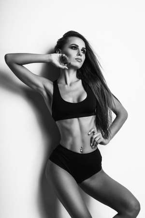 Black and white studio photo of a Girl model with long hair poses in the studio on a light background and raises her arm up bent at the elbow. The girl is dressed in short black shorts and a T-shirt.の写真素材