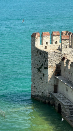 02.08.2024 Italy: Castle Scaligero Tower Above Turquoise Water of lake Garda with Flying Bird Scene in Sirmione.のeditorial素材
