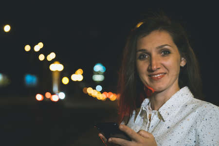 attractive girl in white suit with smartphone in night light reflection standing near copy space...