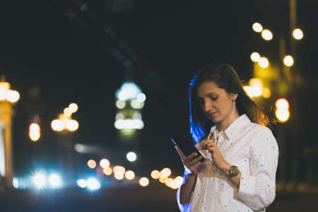 attractive girl in white suit using smartphone in night, , young woman smiling with mobile in handsの写真素材