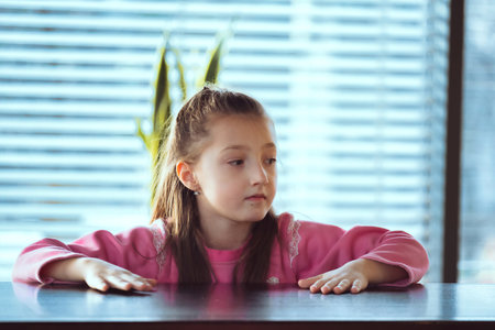 Child sitting on the table looking away to side. Portarit of a little girl in deep thought.の写真素材