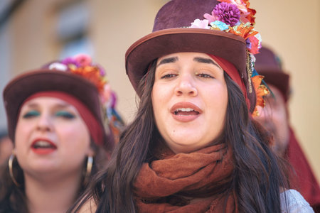 The image shows two women who appear to be singing or performing. They are wearing hats adorned with...