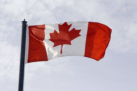 Canadian flag waving in the breeze in the sunshine against a blue skyの写真素材