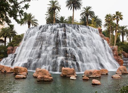 Circular manmade waterfall surrounded by palm trees, rocks, and a poolの写真素材