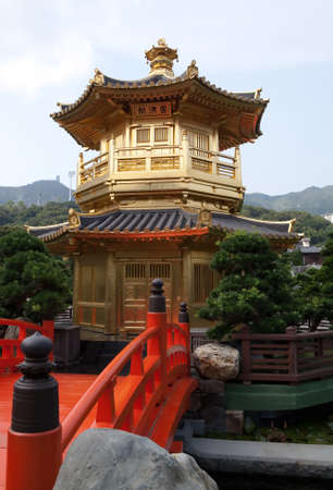 Gold colored pagoda surrounded by water with an orange bridge leading to it の写真素材