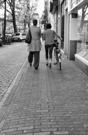 Pedestrian and cyclist walking down a cobblestone sidewalk in Amsterdam, The Netherlandsの写真素材