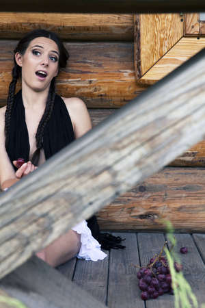 Eighteen girl sitting near a wooden house. Grape on the floorの写真素材