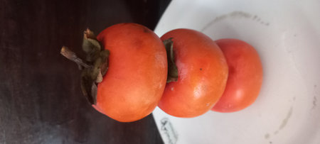 Ripe persimmon fruit on a white plate in the kitchenの写真素材