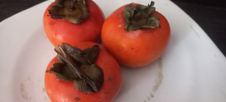 Ripe persimmons on a white plate on a black backgroundの写真素材