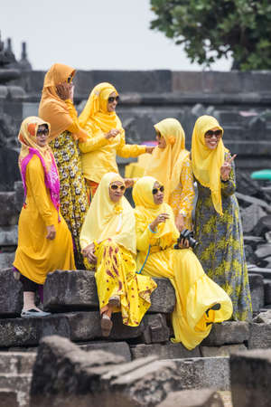 YOGYAKARTA, INDONESIA - CIRCA SEPTEMBER 2015: Women wearing hijab and yellow traditional dresses sit on the ruins of Prambanan templeのeditorial素材
