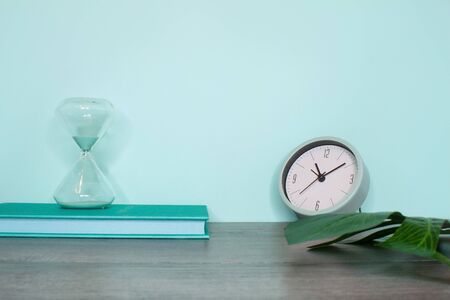 Side view of a still life. Gray wooden table and turquoise wall. Monstera leaf, turquoise book and a...