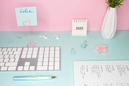 Side view of a business still life. Work place for woman. Cute mint and pink colors and accessories. Keyboard, calendar, vase with flowers and notepadの写真素材