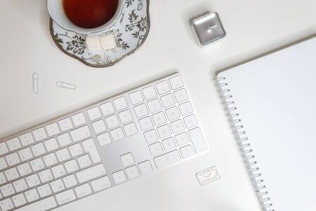 Flat lay of workplace with blank notepad, tea cup and keyboard on white backgroundの写真素材