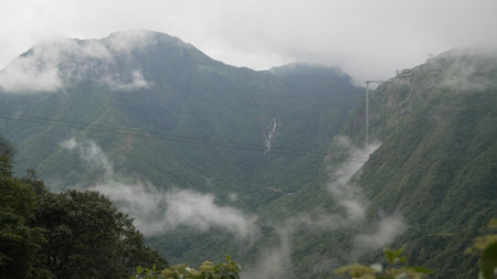 Sa Pa, Vietnam - July 26th 2025: Dense green mountains partially covered by mist with visible cable car lines stretching across the valley.のeditorial素材