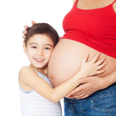 Smiling boy holding mother's belly with hands and listening over white backgroundの写真素材