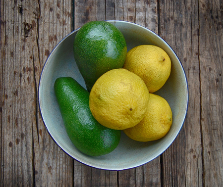 Avocado pears and lemons in a bowl, wood background