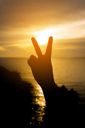 Silhouette Hand with two fingers concept of victory with sunset sea blackground.の写真素材