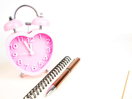 Pink alarm clock in the form of heart with notebook and pen isolated on white background.の写真素材