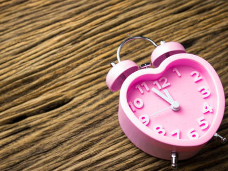 Pink alarm clock in the form of heart on wooden background.の写真素材