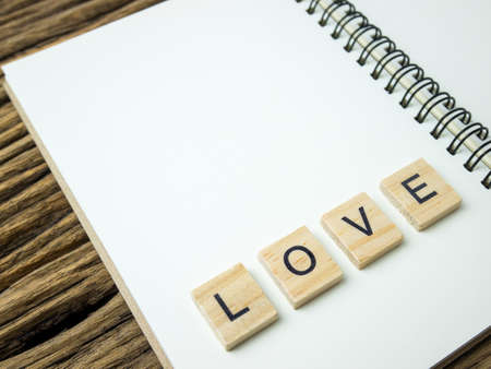 LOVE word in wooden cube and Notebook and pen on wooden blackground, Valentine's Day.の写真素材