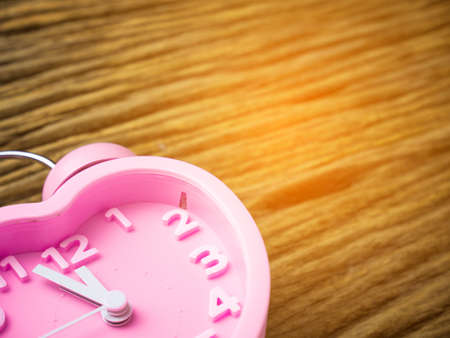 Pink alarm clock in the form of heart on wooden background.の写真素材