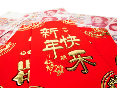 Chinese red envelopes over Chinese money hundred yuan banknotes pile isolated on white background. Chinese text on envelope meaning Happy Chinese New Year.の写真素材