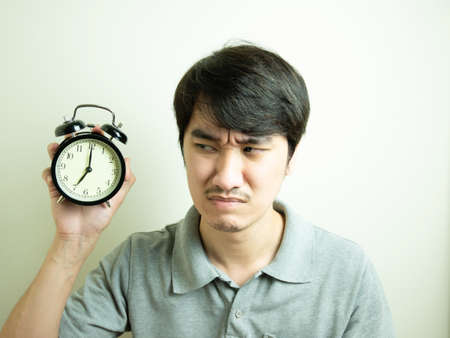 Asian young man with alarm clock in hand at 7 o'clock in the morning.の写真素材