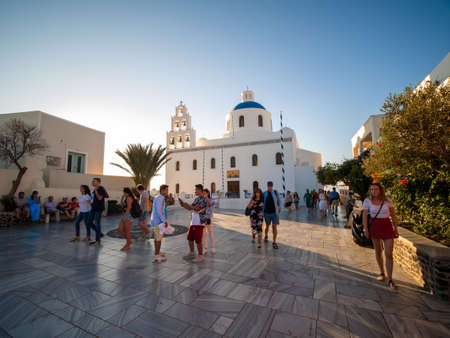 SANTORINI, GREECE JULY. 28, 2019 Traveler Crowd at White Christian church with domes, bells and sunset.のeditorial素材