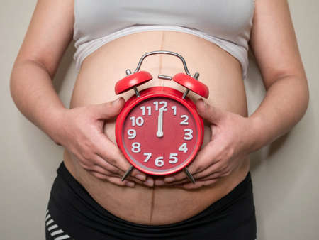 Close Up Of Pregnant Woman Holding red alarm clock.の写真素材