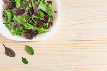 Plate with salad greens on a wooden background. Background for a banner of cooking, restaurant, cafe. Plate of salad greensの写真素材