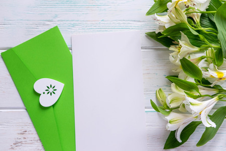 Mock up blank paper and envelope on dark wooden background with natural flowers of white color. Blank, frame for text. Greeting card design with flowers. Aalstroemeria on wooden background.の写真素材