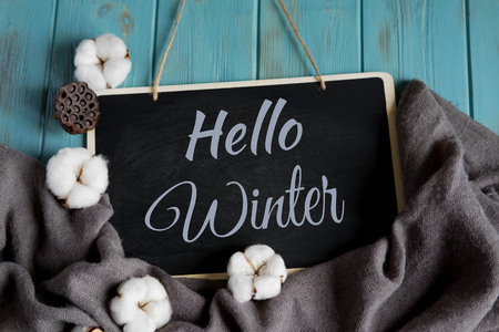 Hello winter postcard. Winter banner with warm gray shawl, cotton flowers on a blue backgroundの写真素材
