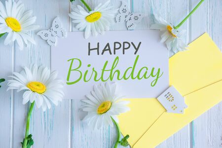 Happy birthday inscription. Natural daisies on a wooden background with the inscription Happy Birthday. Greeting card design. Floral background. Flat lay, top view.の写真素材