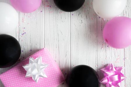Design frame for birthday card background. Pink, white and black balloons with a gift box on a light wooden background.の写真素材