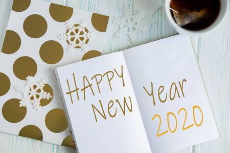Sample layout of New Years 2020 greetings with snowflakes, open notebook, cup of tea on a light wooden background. Frame for text. Blog post publication, promo campaign, email newsletter templateの写真素材