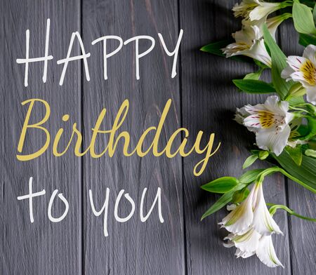 Greeting card with the inscription happy birthday. Congratulatory greeting to the girl, mother with flowers and a gift on a wooden backgroundの写真素材