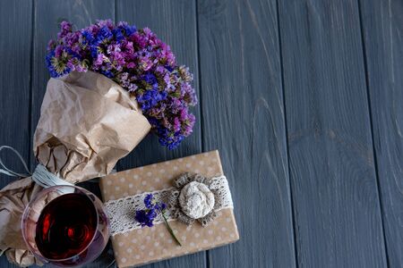 A glass of red wine close-up along with a bouquet of wildflowers and gift boxes on a dark wooden background. Birthday greeting card banner design.の写真素材