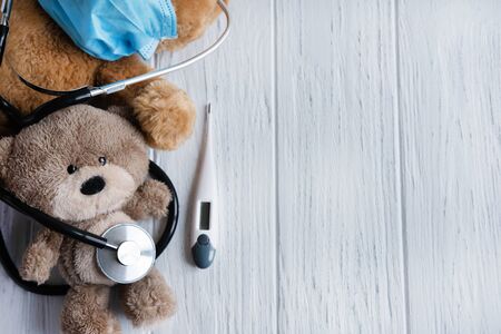 Conceptual background on the topic of viral diseases in children. Temperature, runny nose, flu, coronovirus. Children's clinic for the treatment of viruses. Virus masked toy bear.の写真素材