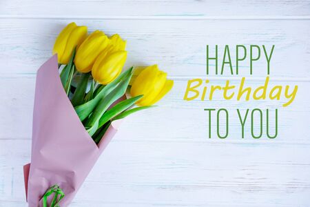 Birthday greeting card with yellow tulips and the inscription on a light wooden background. Greeting card for posting, blog posting for a birthdayの写真素材