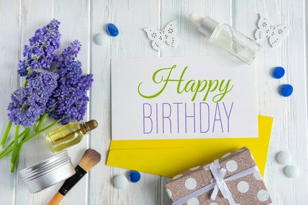 Spring greeting beauty birthday card. Makeup brush, gift, lilac flowers on a light wooden backgroundの写真素材