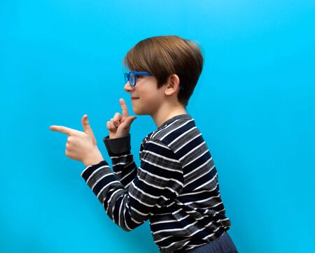 The cheerful boy of 9 years points a hand on something. Smiling boy with glasses stands sidewaysの写真素材