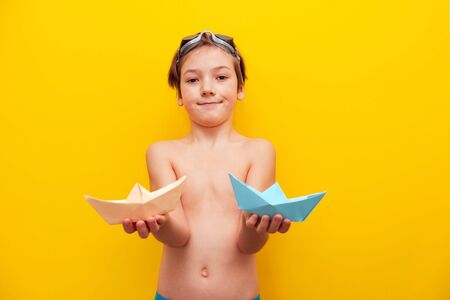 Closeup boy holds paper boats in front of him on an orange background. Sea holidays and travel background. Traveling in the summer at sea.の写真素材