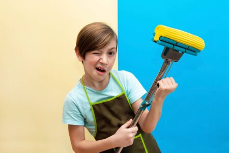 Close-up boy winks with a mop in his hands. Mop like a guitar in the hands of a boy. House cleaning to the music.の写真素材